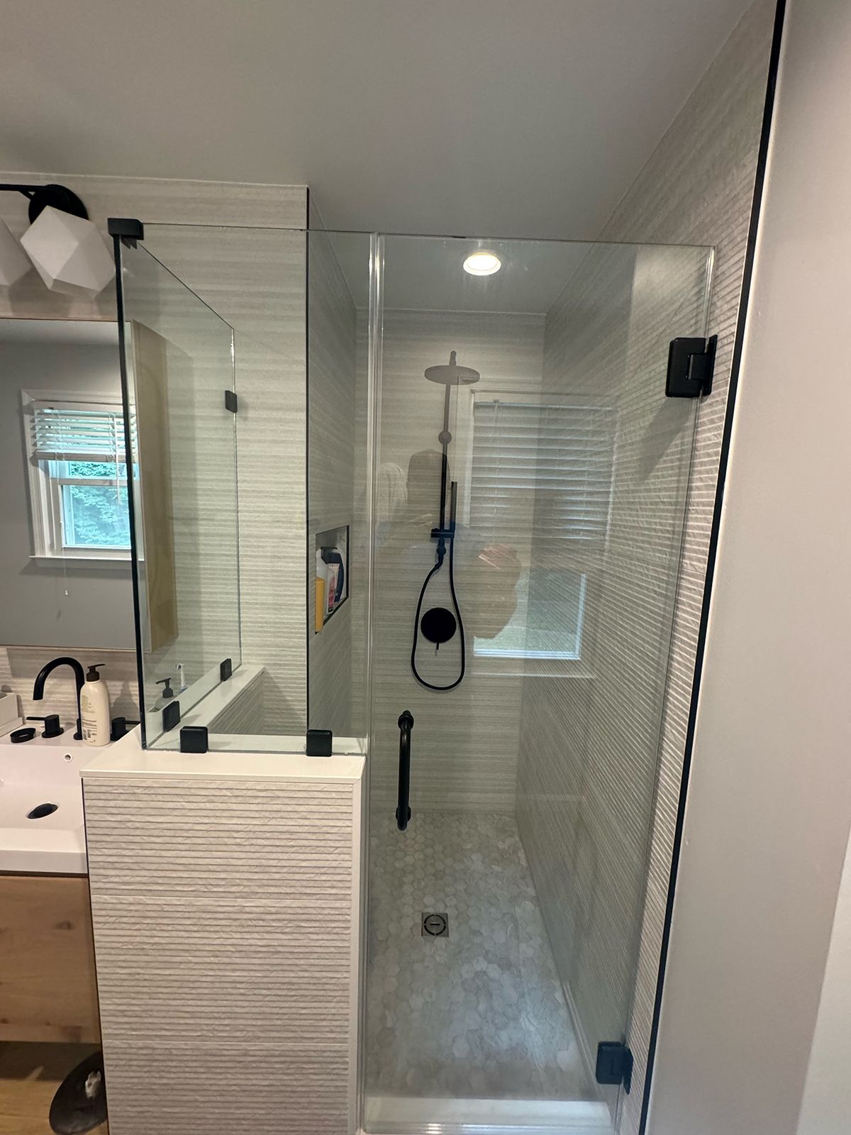 A glass-enclosed shower with black fixtures and textured white tile, positioned next to a bathroom vanity.