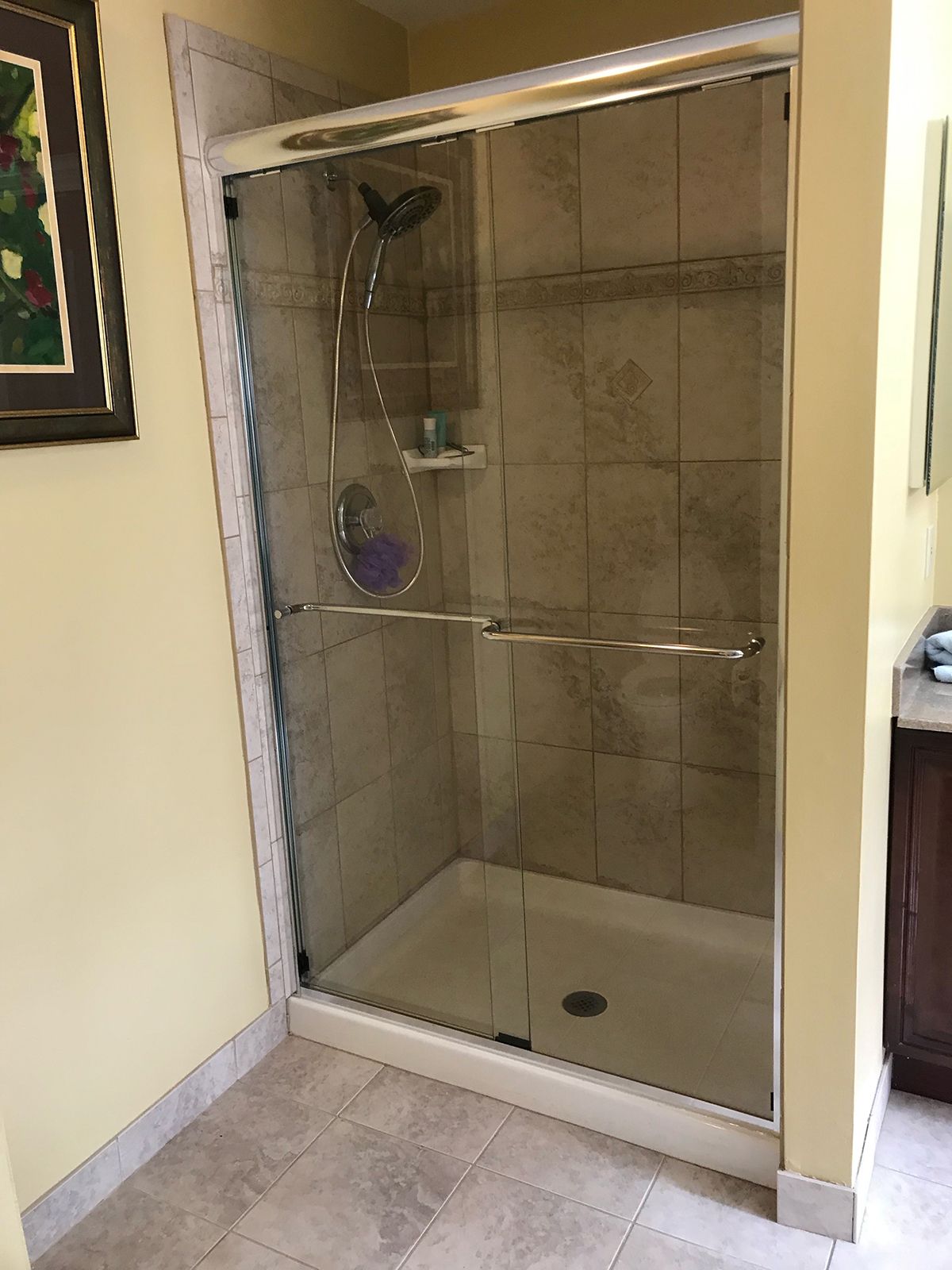 A shower stall with a glass sliding door, tan tiled walls, and a beige shower base in a bathroom with yellow walls.