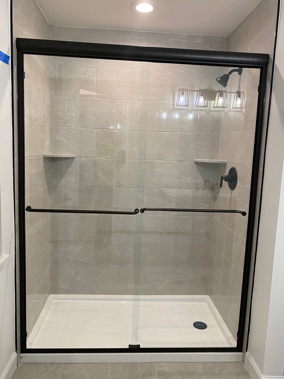 A walk-in shower with light gray tiled walls, a white floor pan, and black-framed sliding glass doors.