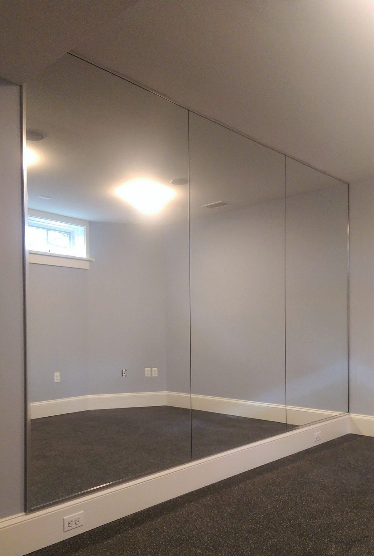 Three floor-to-ceiling mirrors mounted side-by-side on a gray wall in a room with dark carpet and white baseboards.