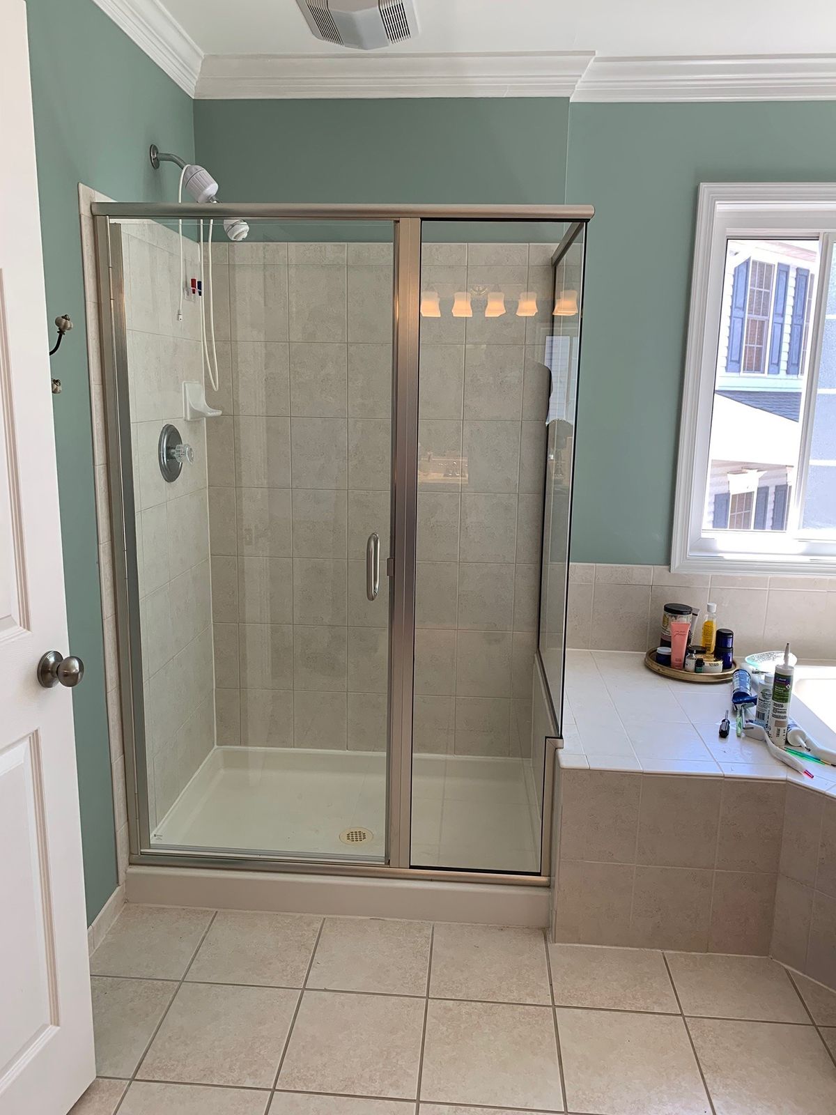 A bathroom featuring a glass shower stall with tiled walls, sage green painted walls, and a white tiled floor.