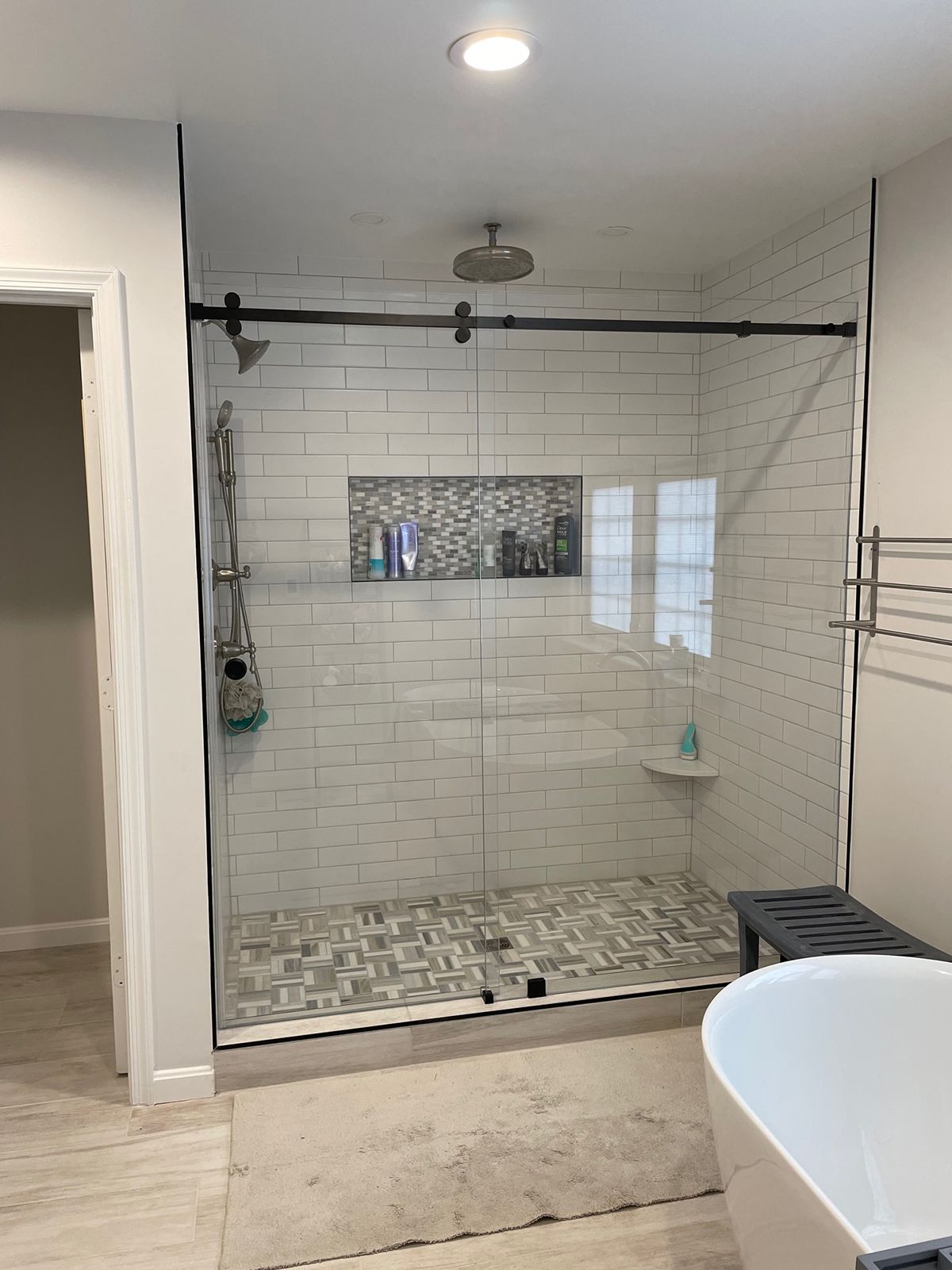 A walk-in shower with white subway tile walls, a decorative mosaic inset shelf, and a sliding glass door.