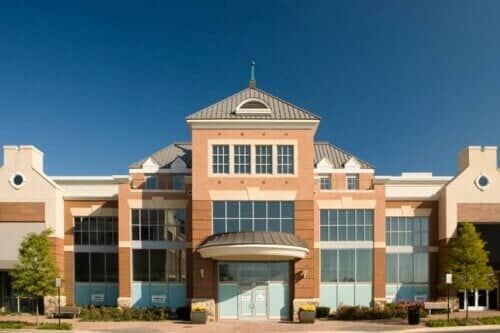 Multi-story brick and tan building with arched entrance and large windows under a clear blue sky.