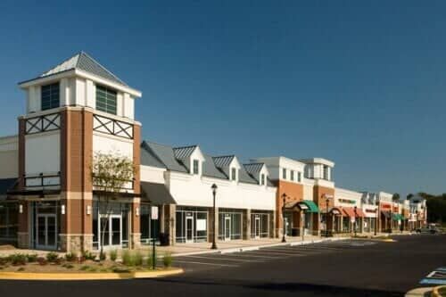 Shopping plaza with a multi-story tower and multiple store fronts on a sunny day.