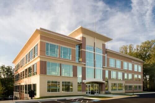 Three-story beige and brick office building with large windows and a glass entrance.
