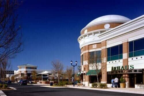 Shopping center exterior with brick buildings, clear blue sky, street, people.