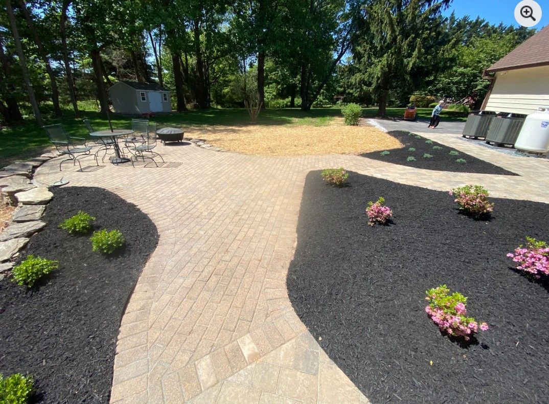 A yard with a gravel path and flower beds with green and pink plants, separated by black mulch.
