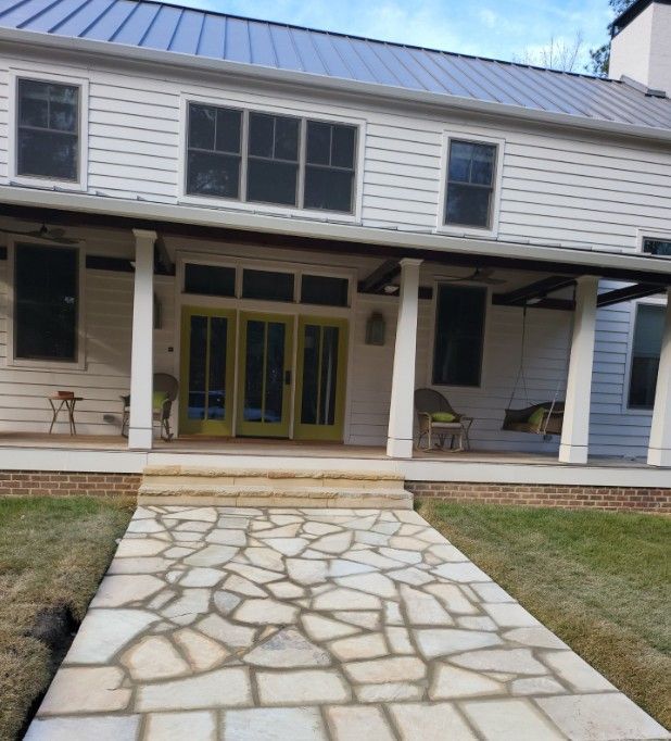 A two-story white house with a stone pathway leading to a covered porch. The front door is yellow.
