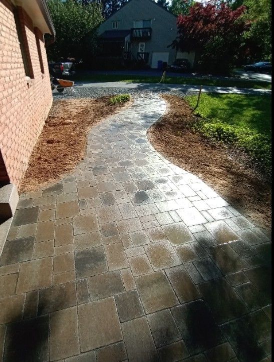 Brick pathway curves along a brick building and through a yard. The pathway is made of interlocking pavers with mulch on either side.
