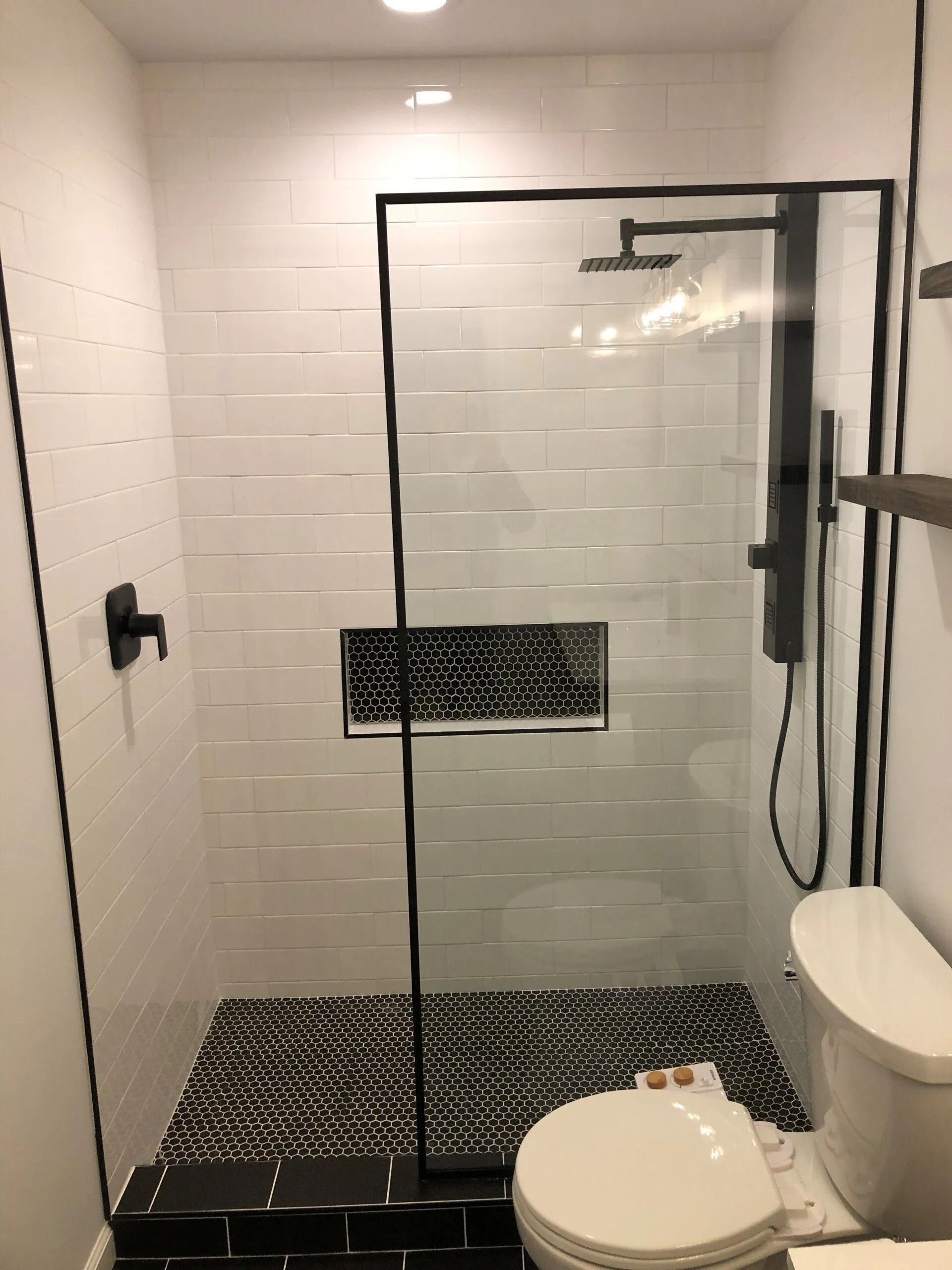 Small black-and-white tiled bathroom with a walk-in shower, glass door, and toilet in the foreground.