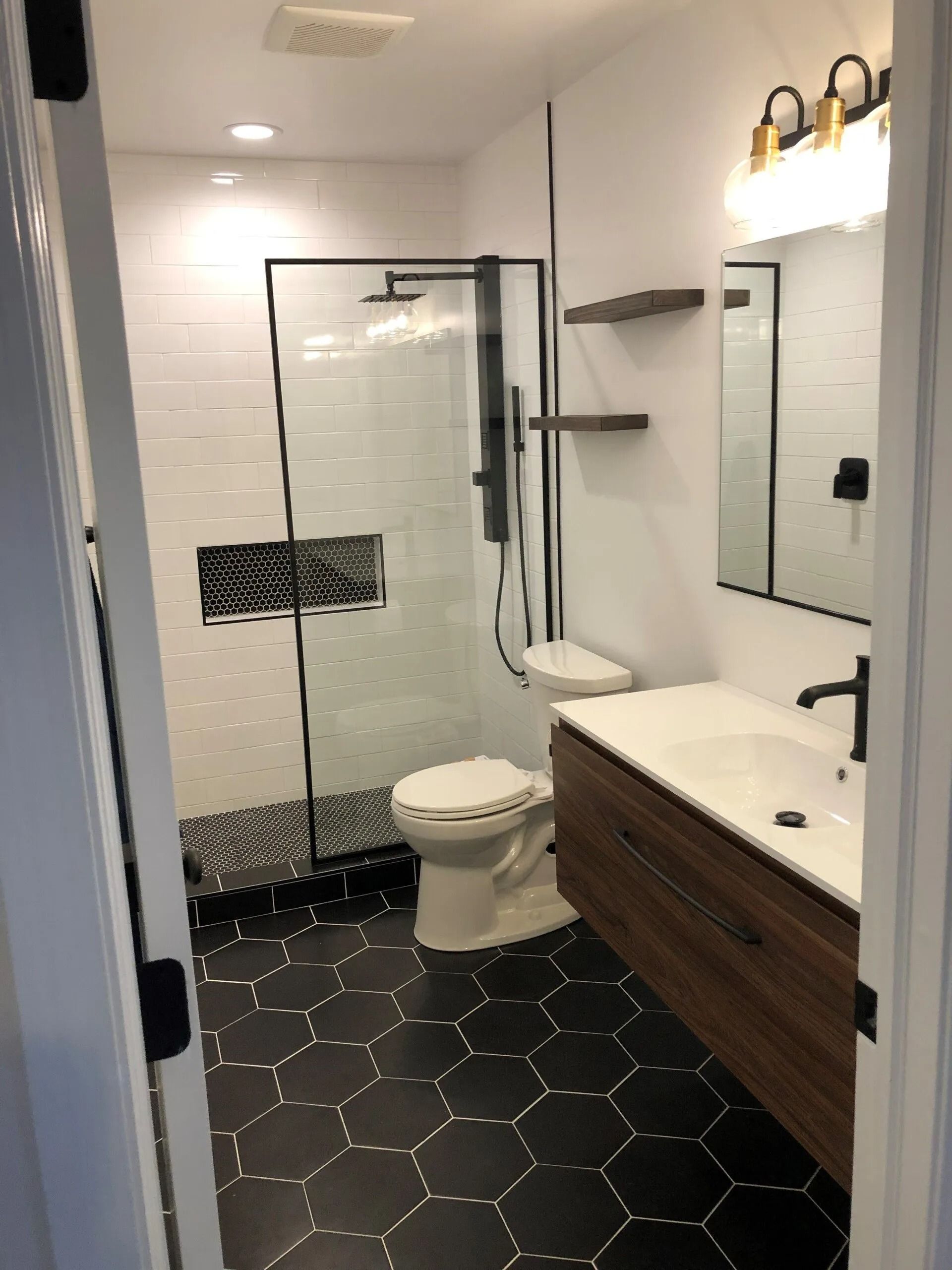 Modern bathroom with hex tile floor, glass shower, toilet, wooden vanity, and large mirror