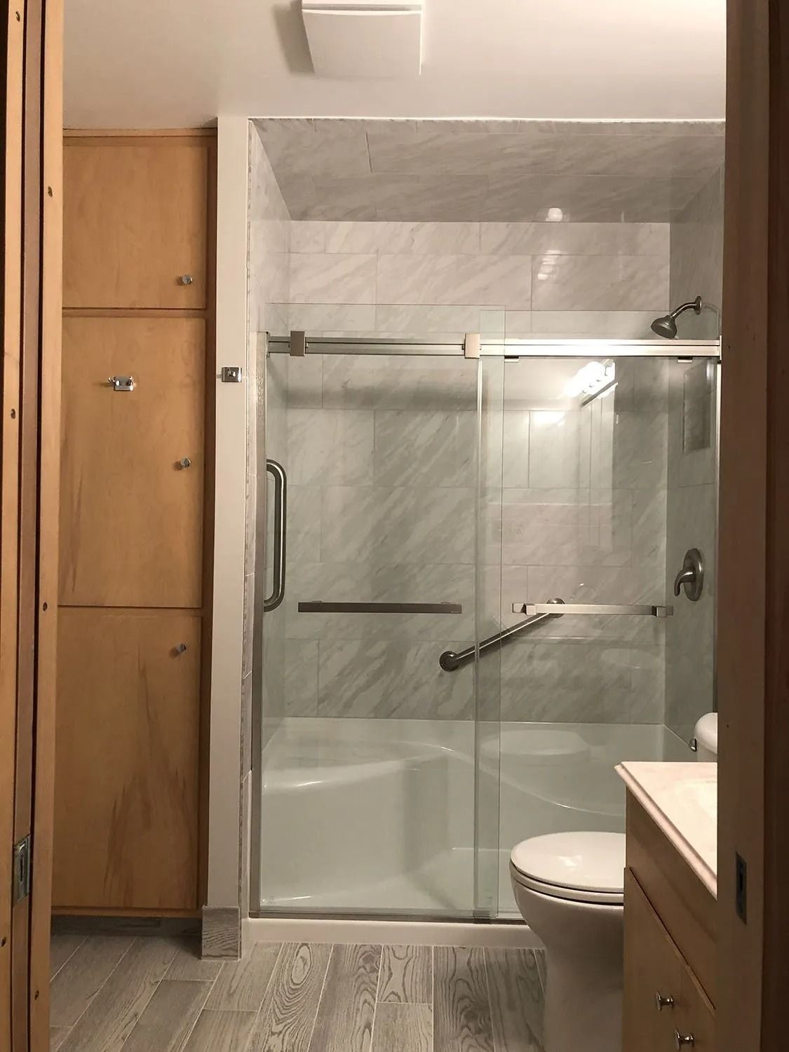Bathroom with a glass shower enclosure, toilet, vanity cabinet, and tall wooden storage cabinet.