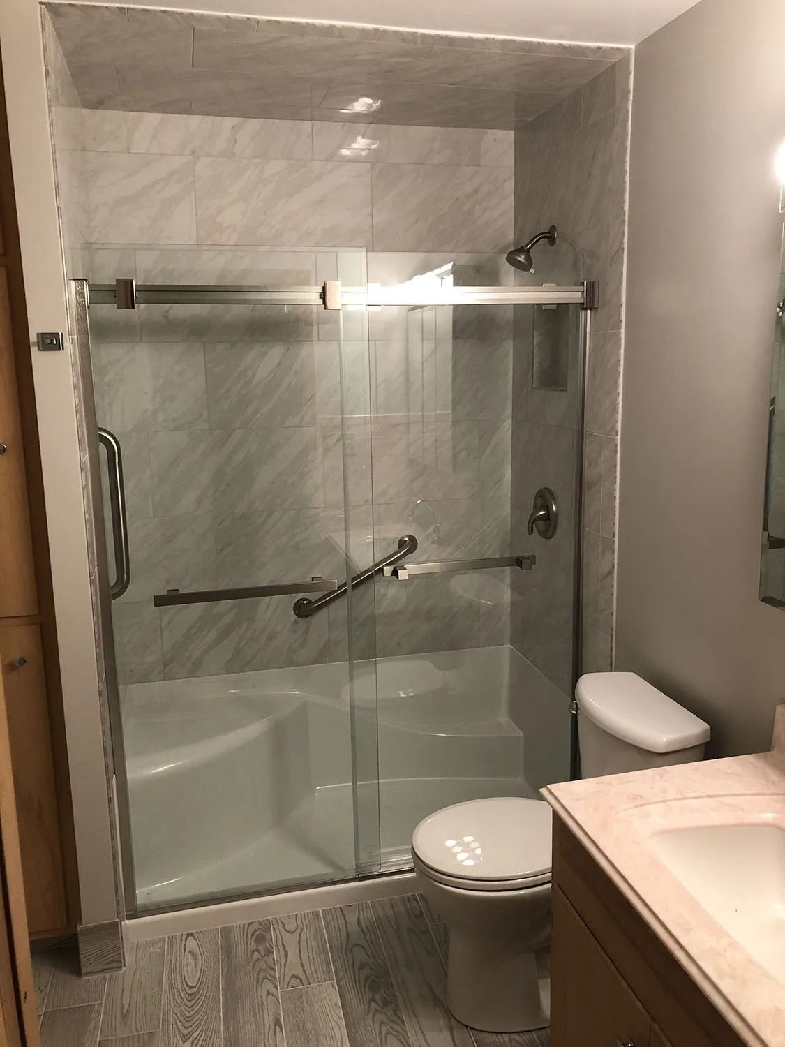 Small bathroom with glass shower, white toilet, and beige countertop sink.