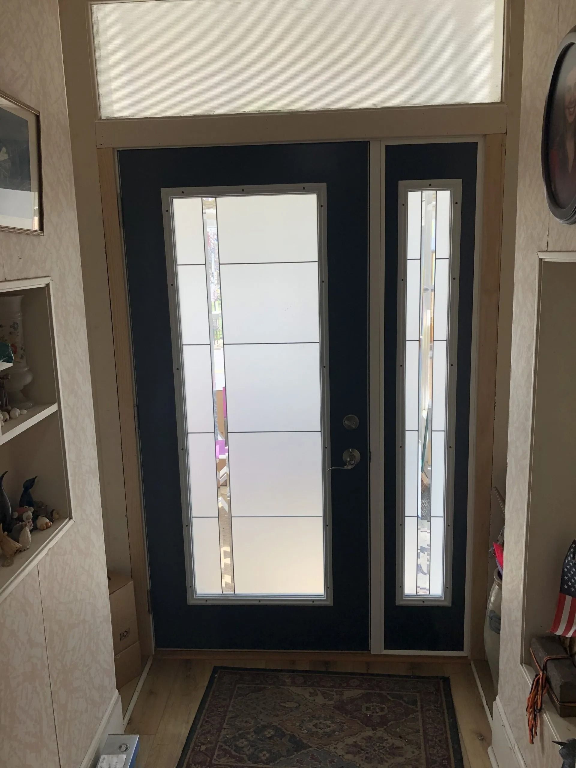 Front entryway with a black door, frosted glass panels, a doormat, and wall shelves