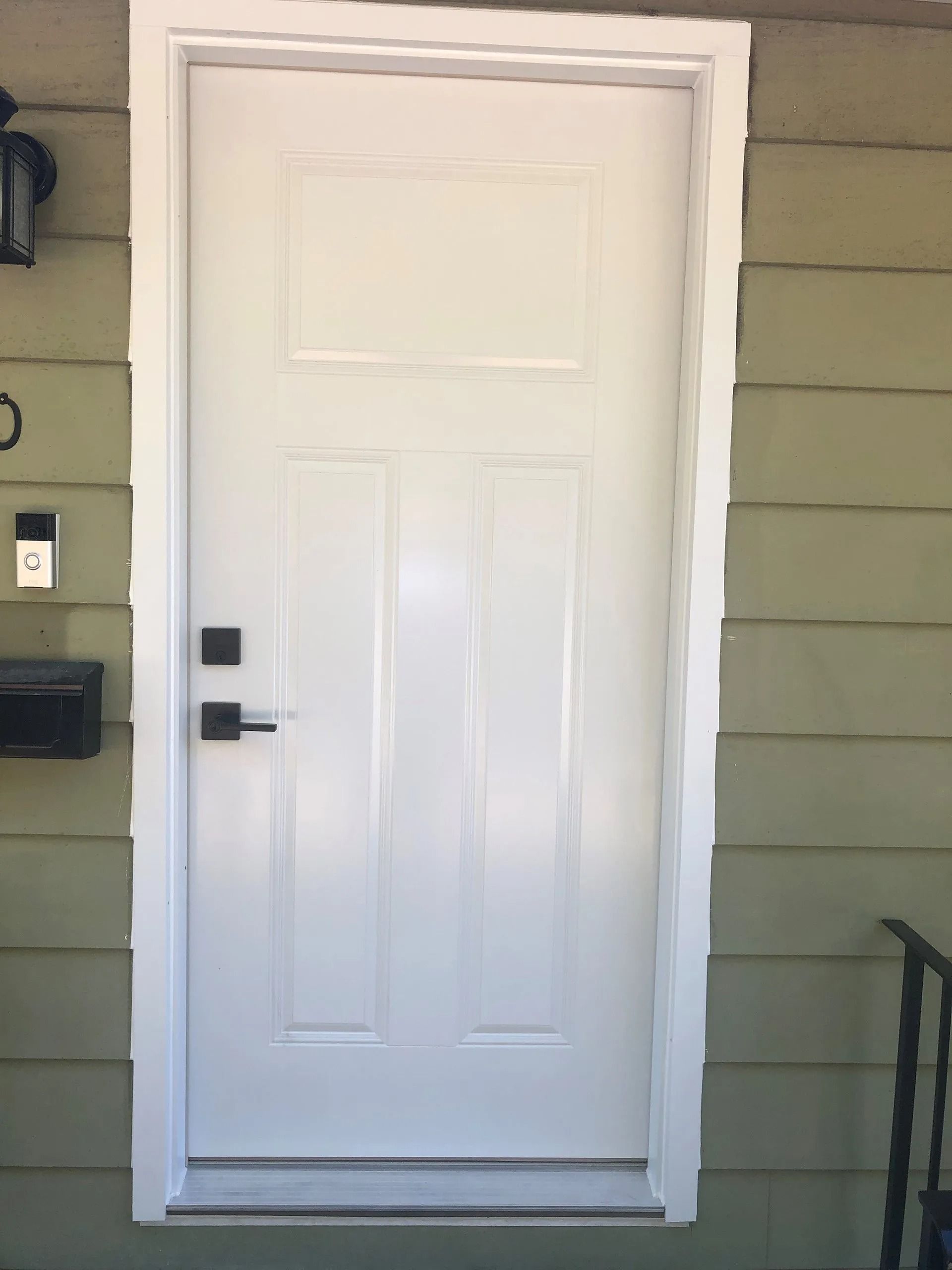 Front door with black handle and mail slot, set in green siding with white trim and small step.
