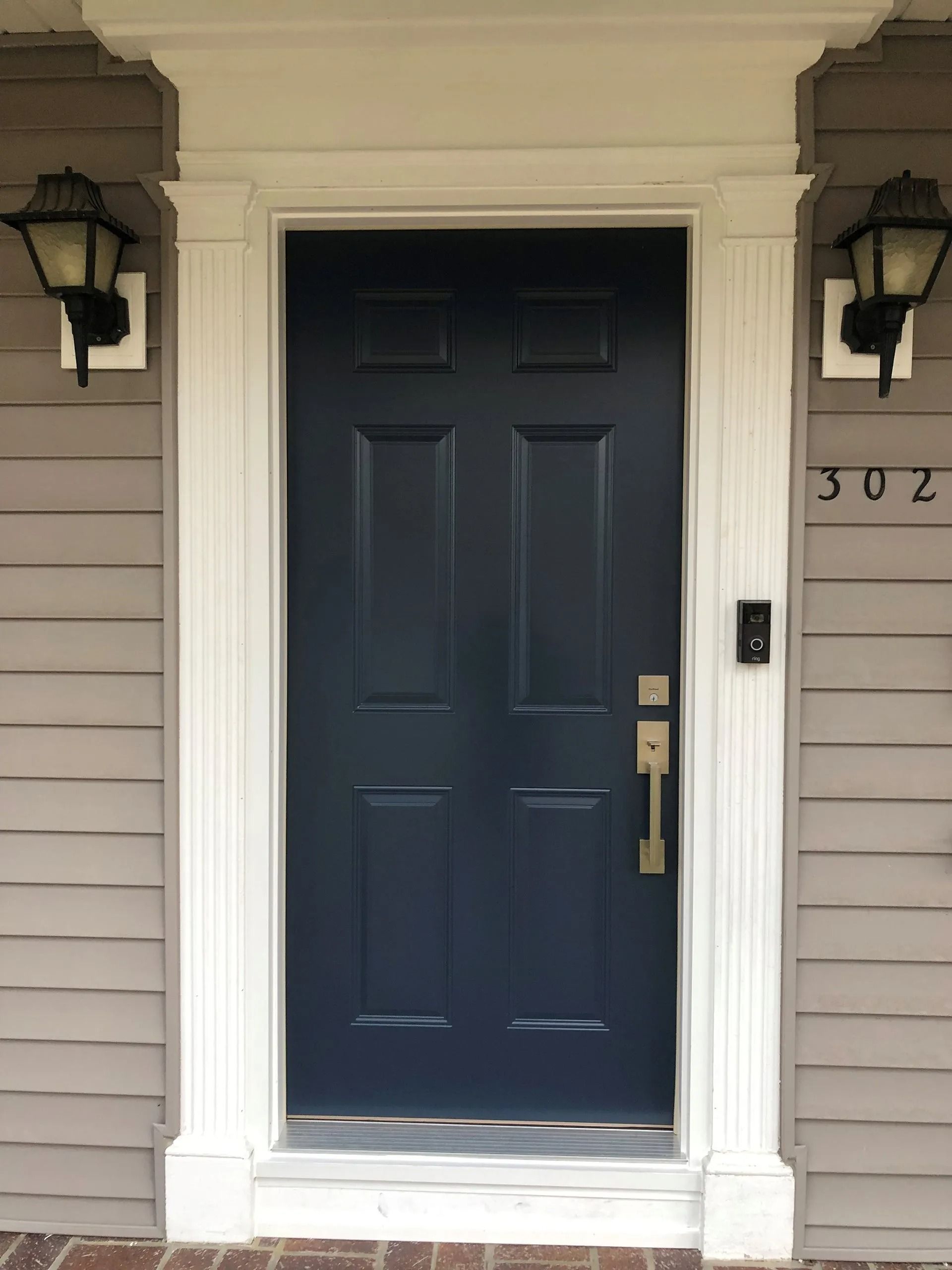 Front door with dark blue panels, brass handle, and house number 302 on a beige home exterior.