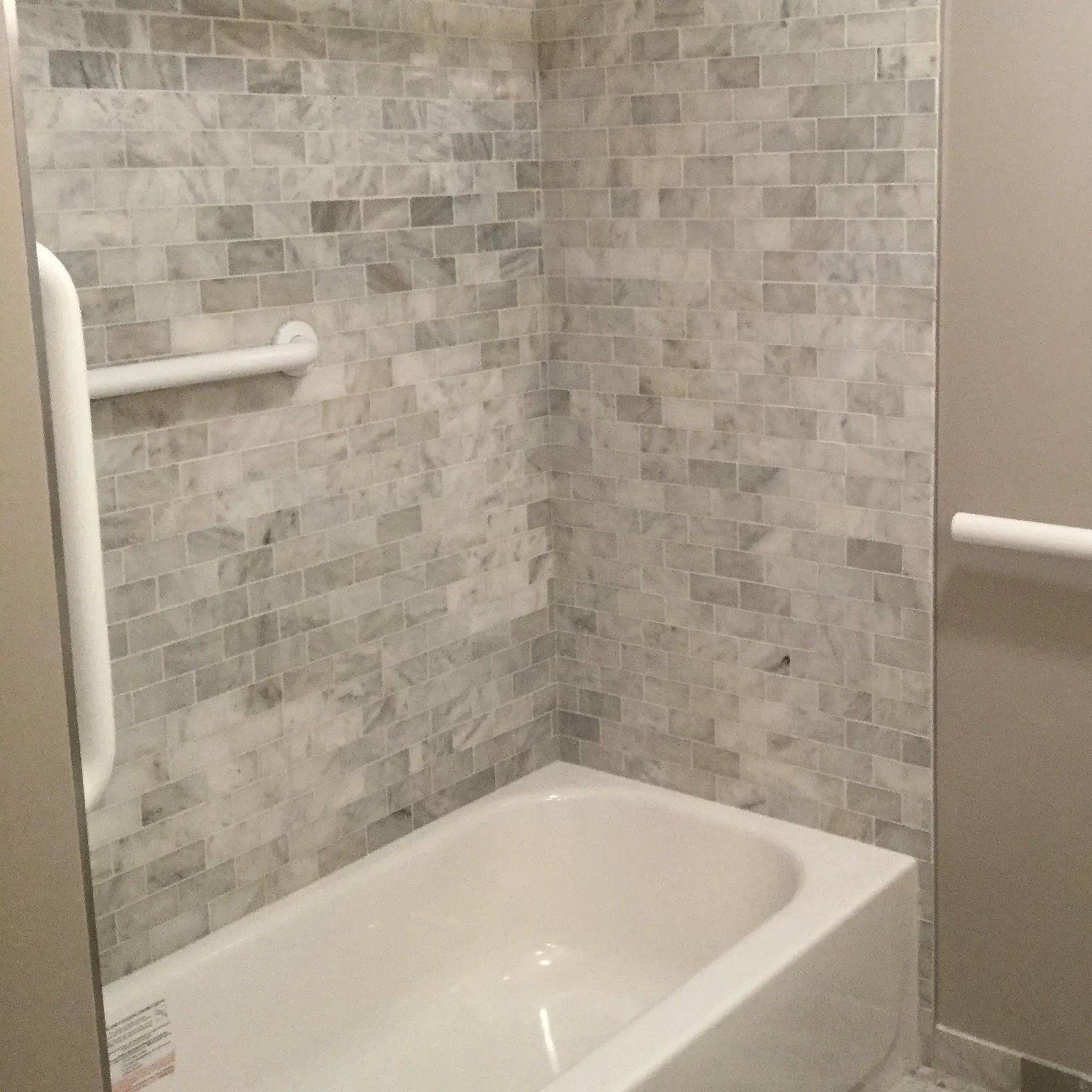 Accessible shower-tub combo with gray tile walls and white grab bars