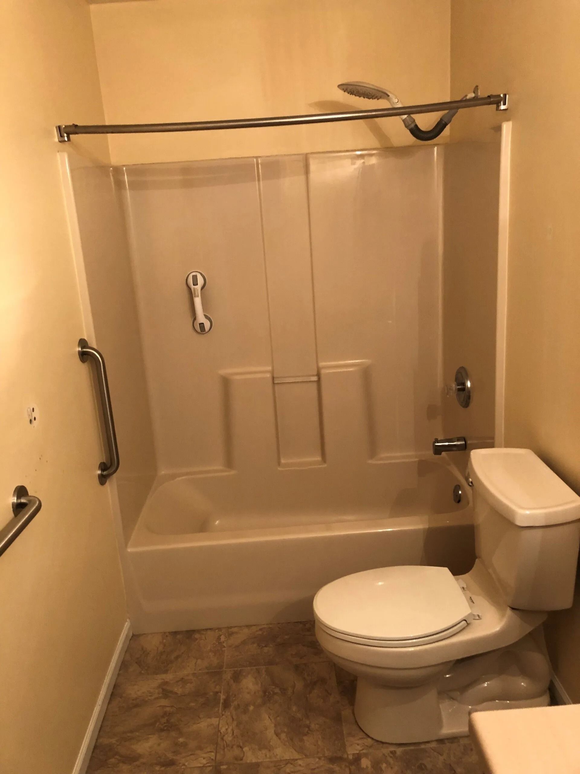 Bathroom with tub-shower combo, toilet, and beige walls in a small accessible-style layout