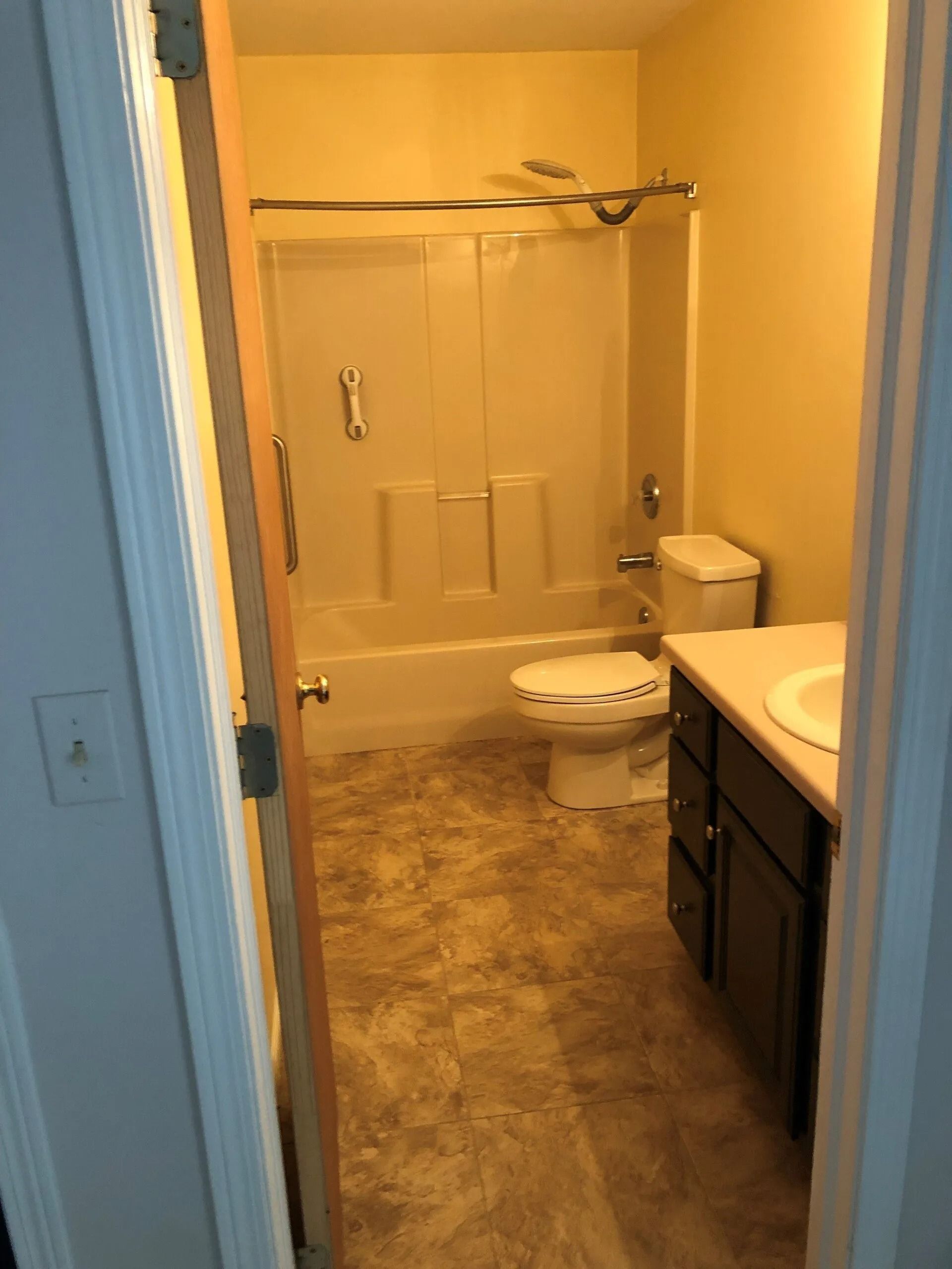 Small bathroom with shower, toilet, and vanity in a narrow hallway view.
