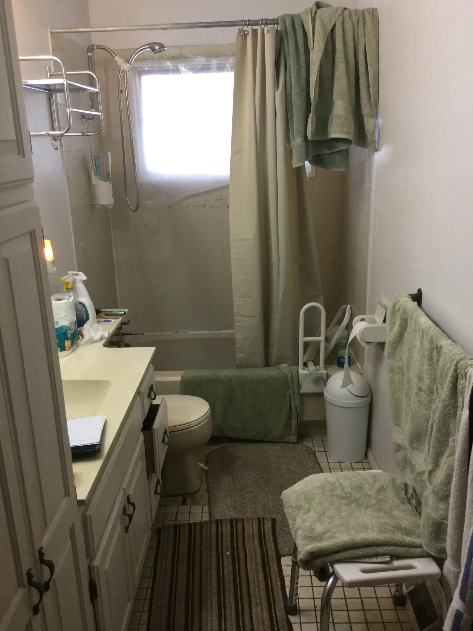 Small bathroom with green towels, shower curtain, vanity, and striped rug.
