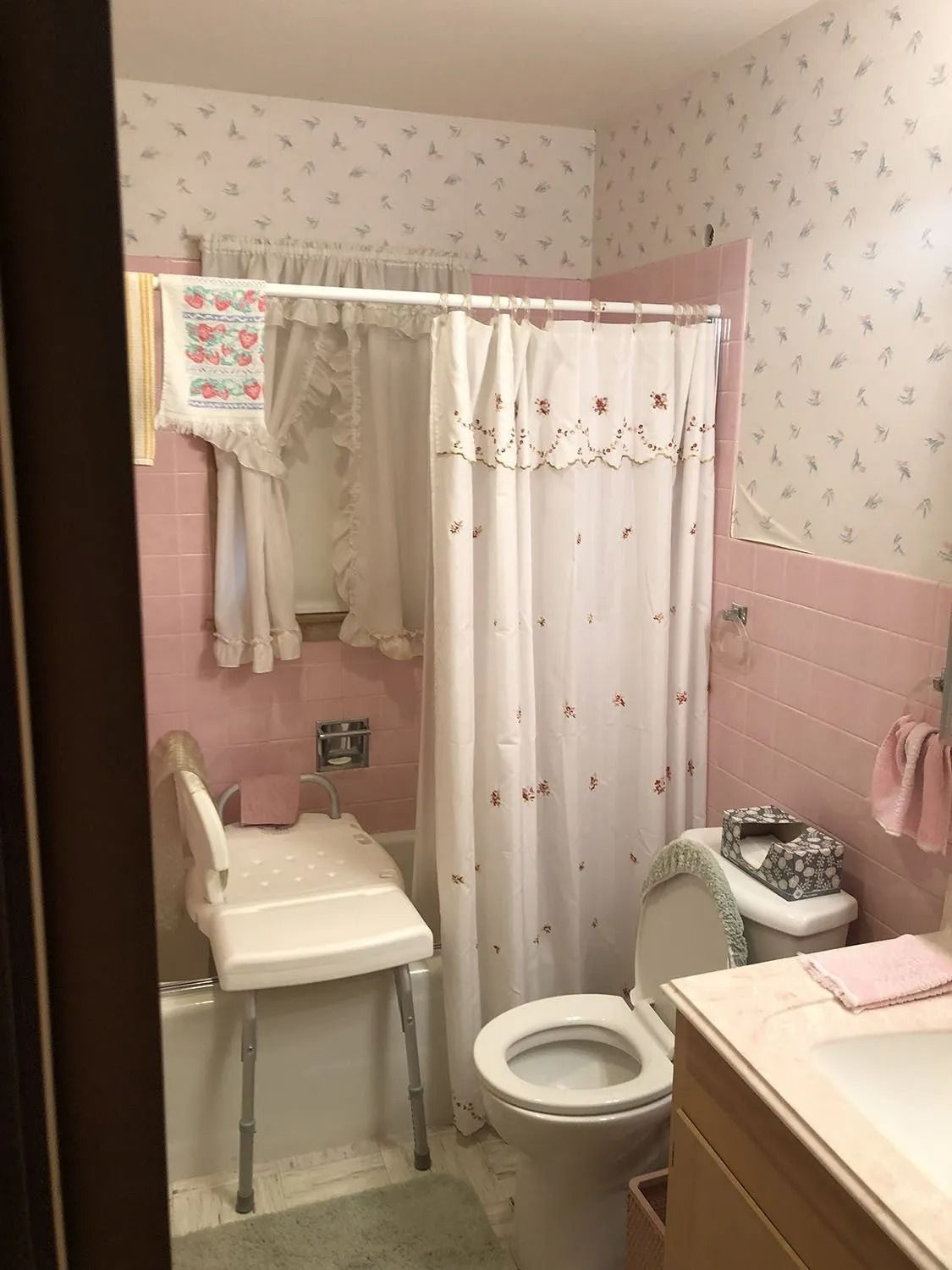Small pink bathroom with shower curtain, toilet, chair, and vanity sink.