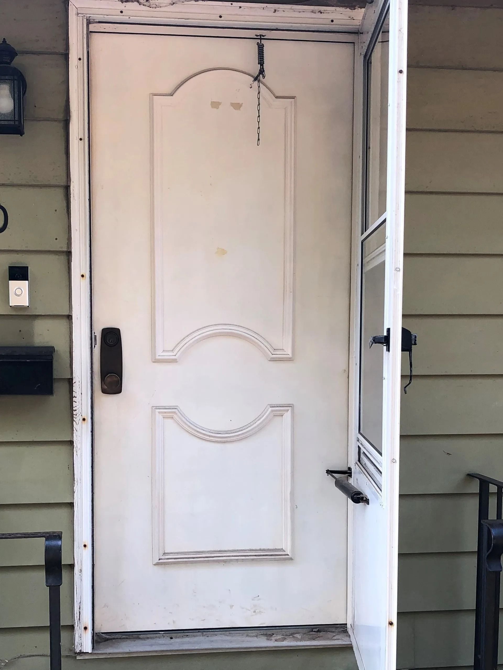 White front door with decorative panels, partly open on a house porch.