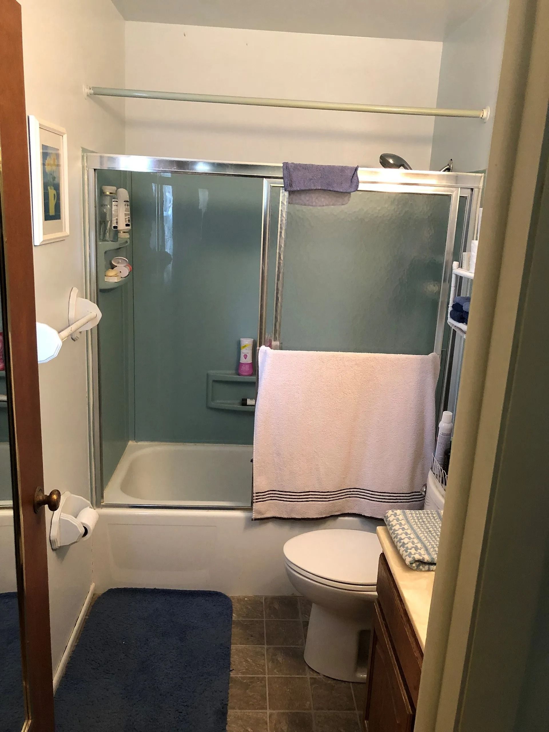 Small bathroom with blue shower curtain, white towel, toilet, and sink cabinet.