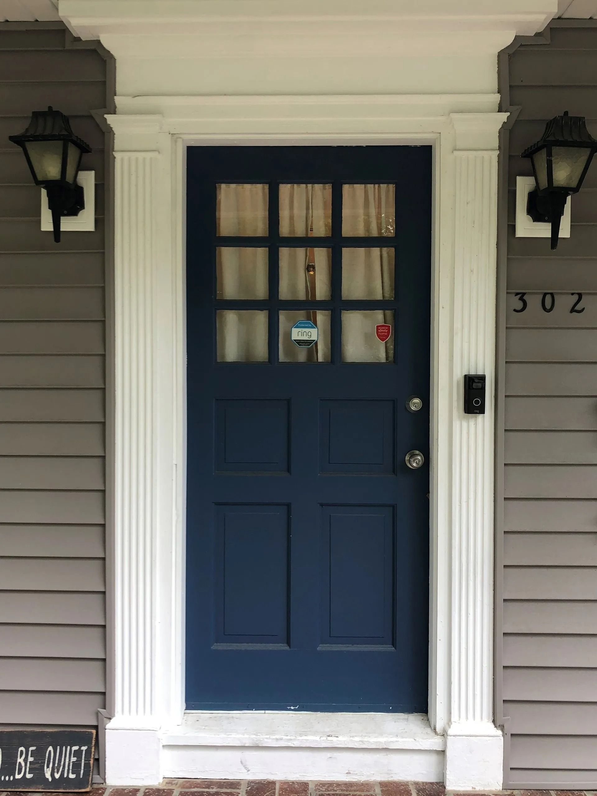 Blue front door with small window panes, framed by white trim and black lanterns
