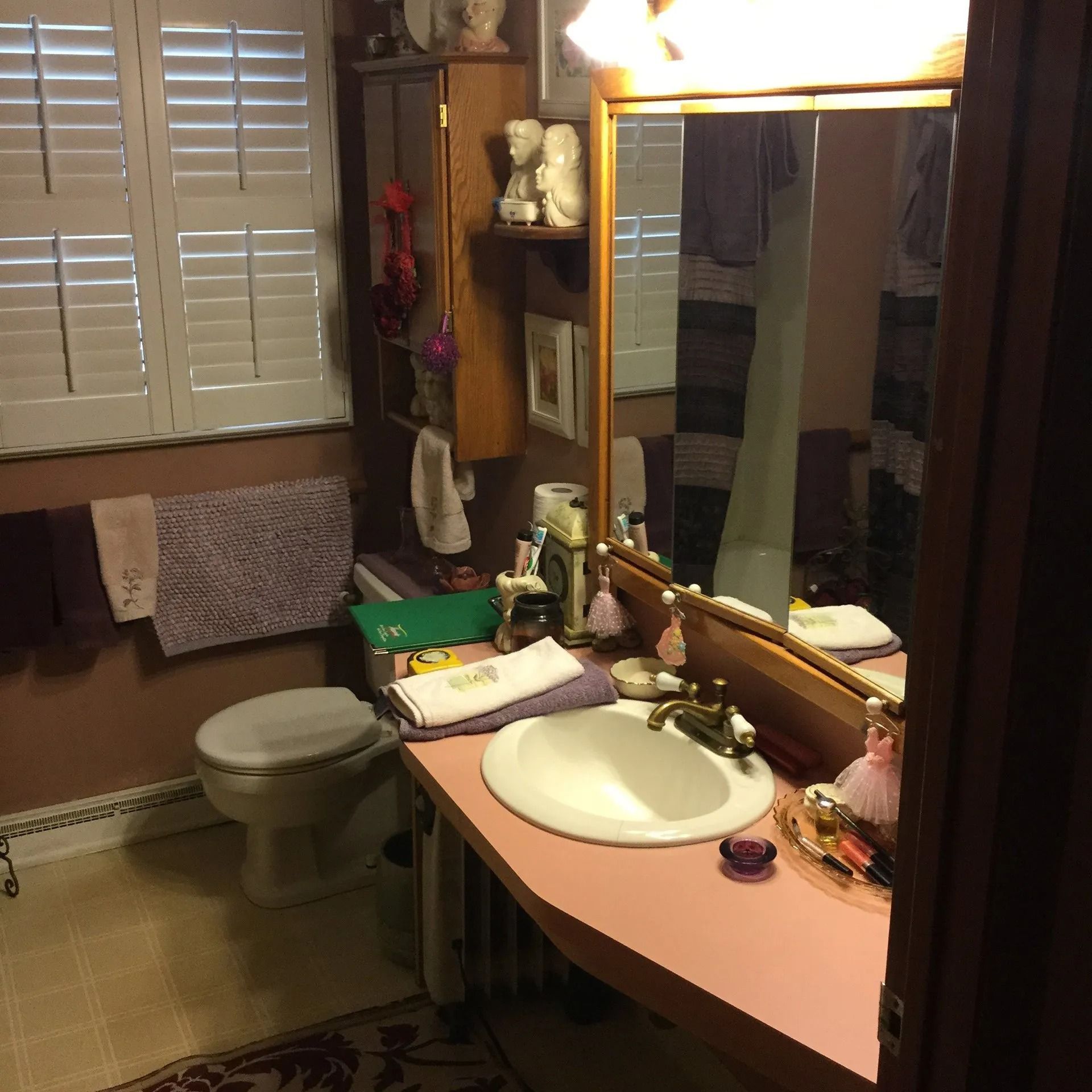 Small bathroom with sink, mirror, toilet, window shutters, and beige tile walls.