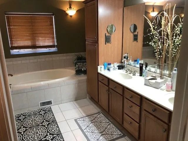 Bathroom with wood vanity, large mirror, soaking tub, and patterned rugs.