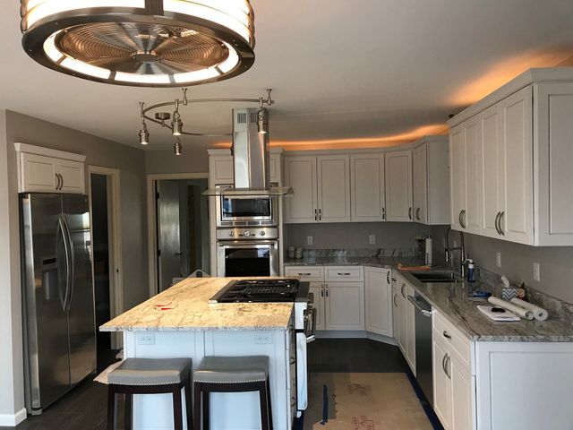 Bright white kitchen with stainless appliances, large island, and modern cabinets under warm ceiling lights