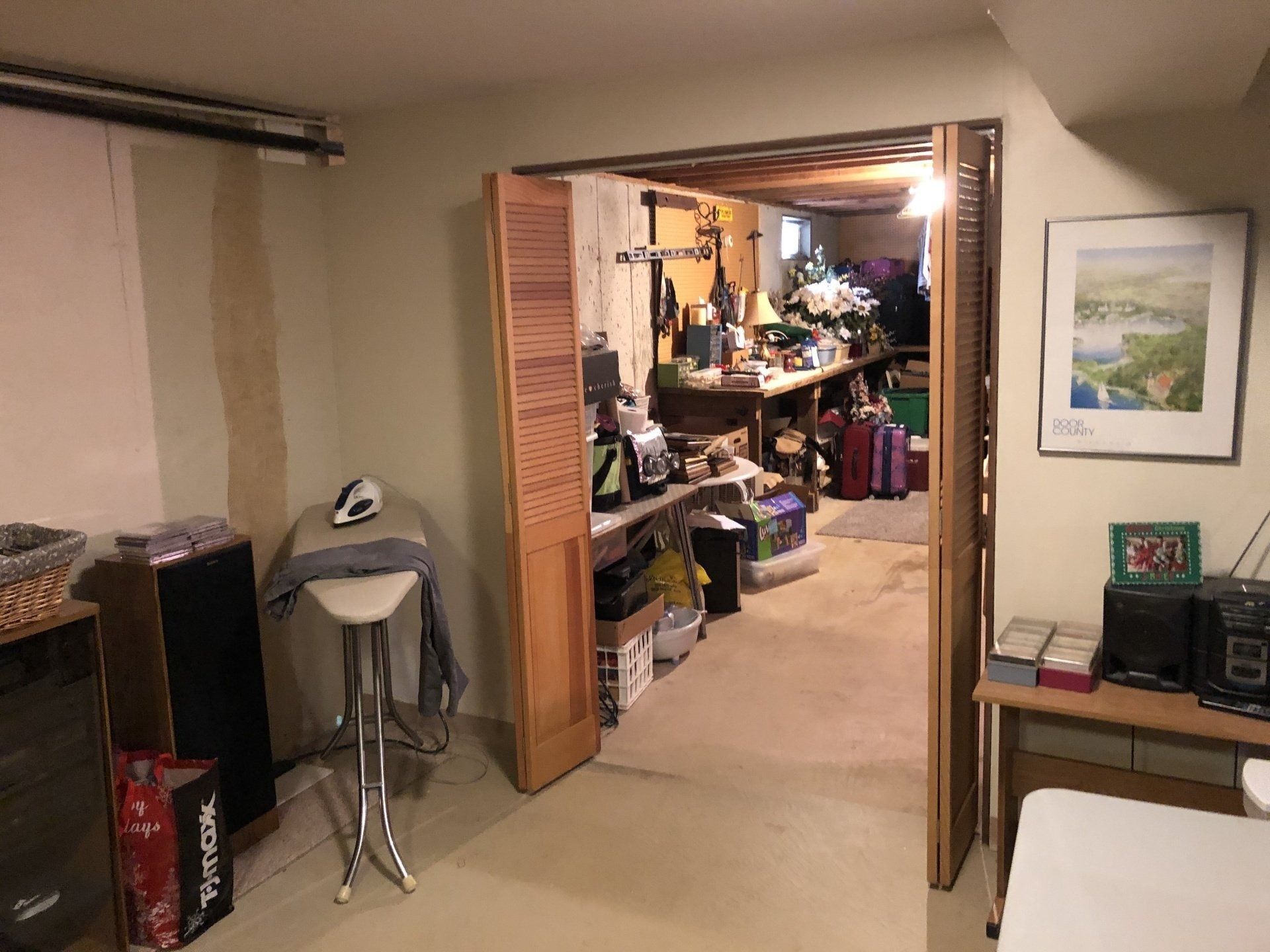 Basement room opening into a cluttered storage area with shelves, boxes, and household items