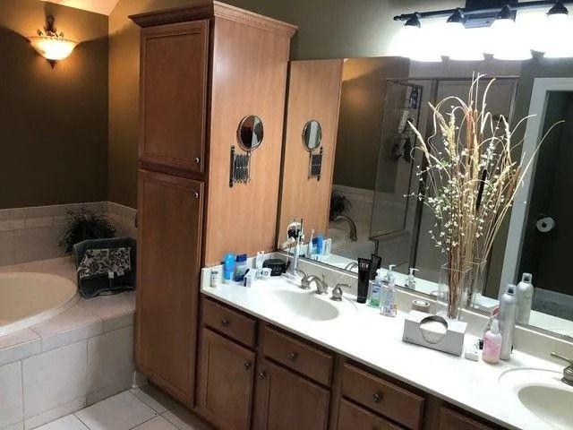 Bathroom with double sink vanity, large mirror, white countertop, and a bathtub beside a dark wall.