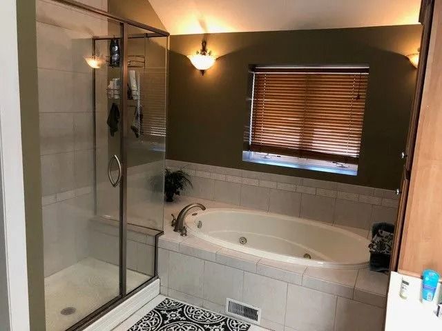 Bathroom with a glass shower, soaking tub, beige tile, and window with wood blinds.
