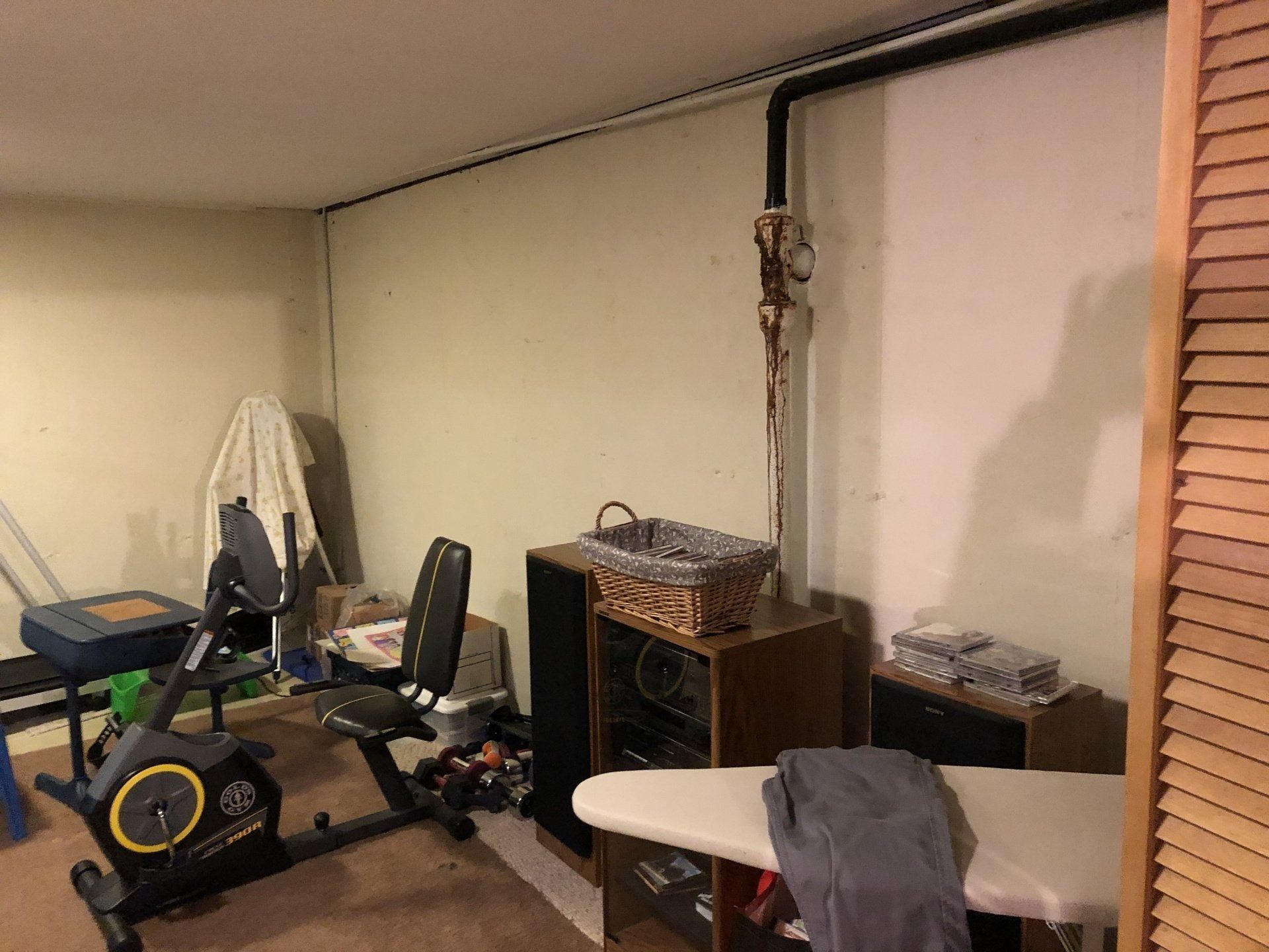 Basement workout area with exercise bikes, an ironing board, and storage shelves along the wall
