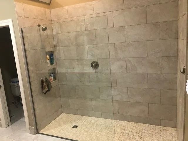 Glass-enclosed tiled walk-in shower with white floor and built-in corner shelves