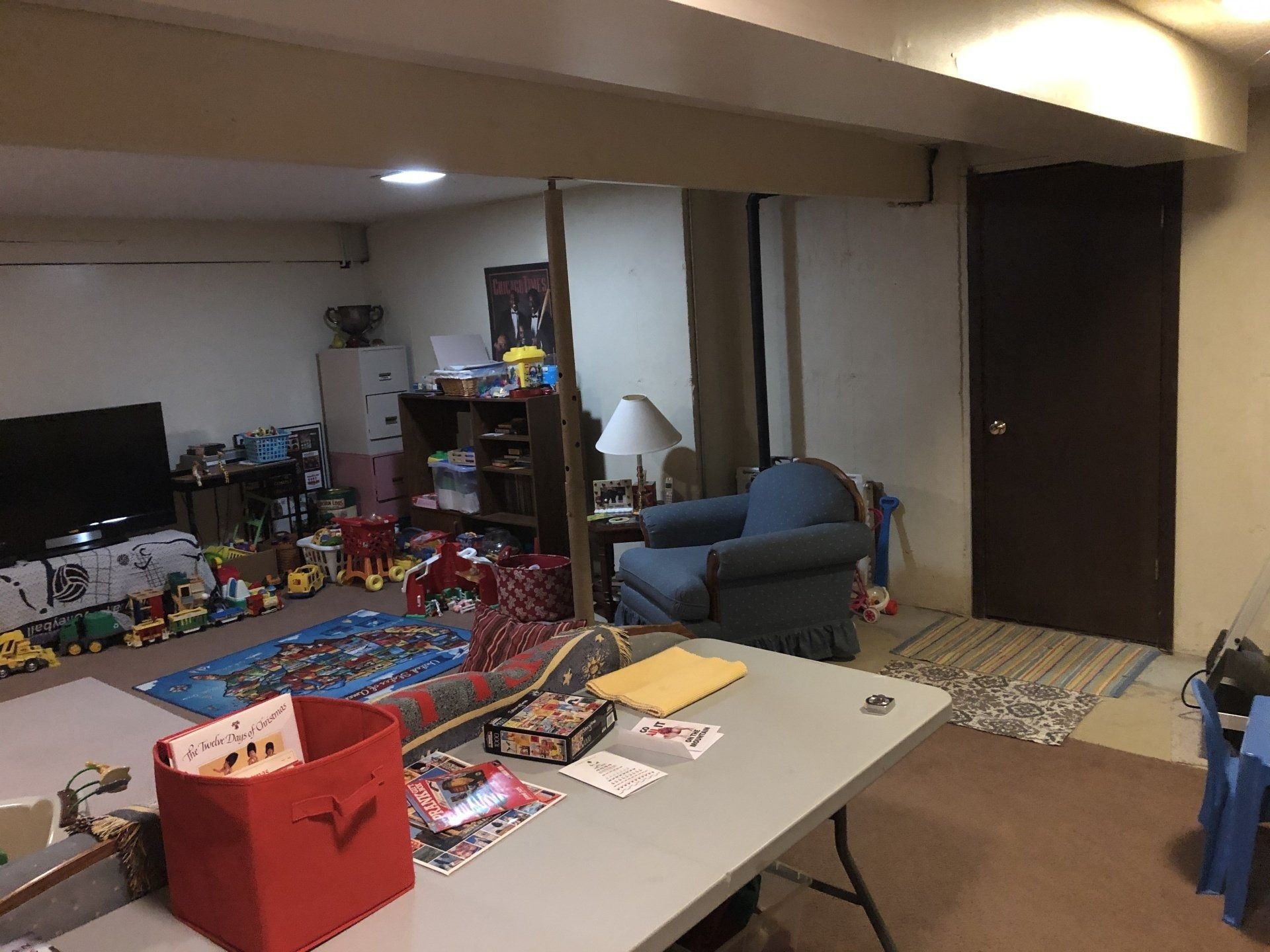 Cluttered basement playroom with toys, a blue chair, and a table in the foreground.