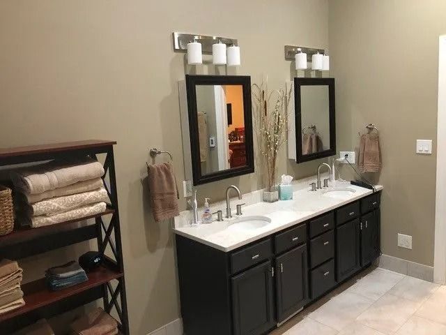 Bathroom vanity with double sinks, black cabinets, and two mirrors on a beige wall.