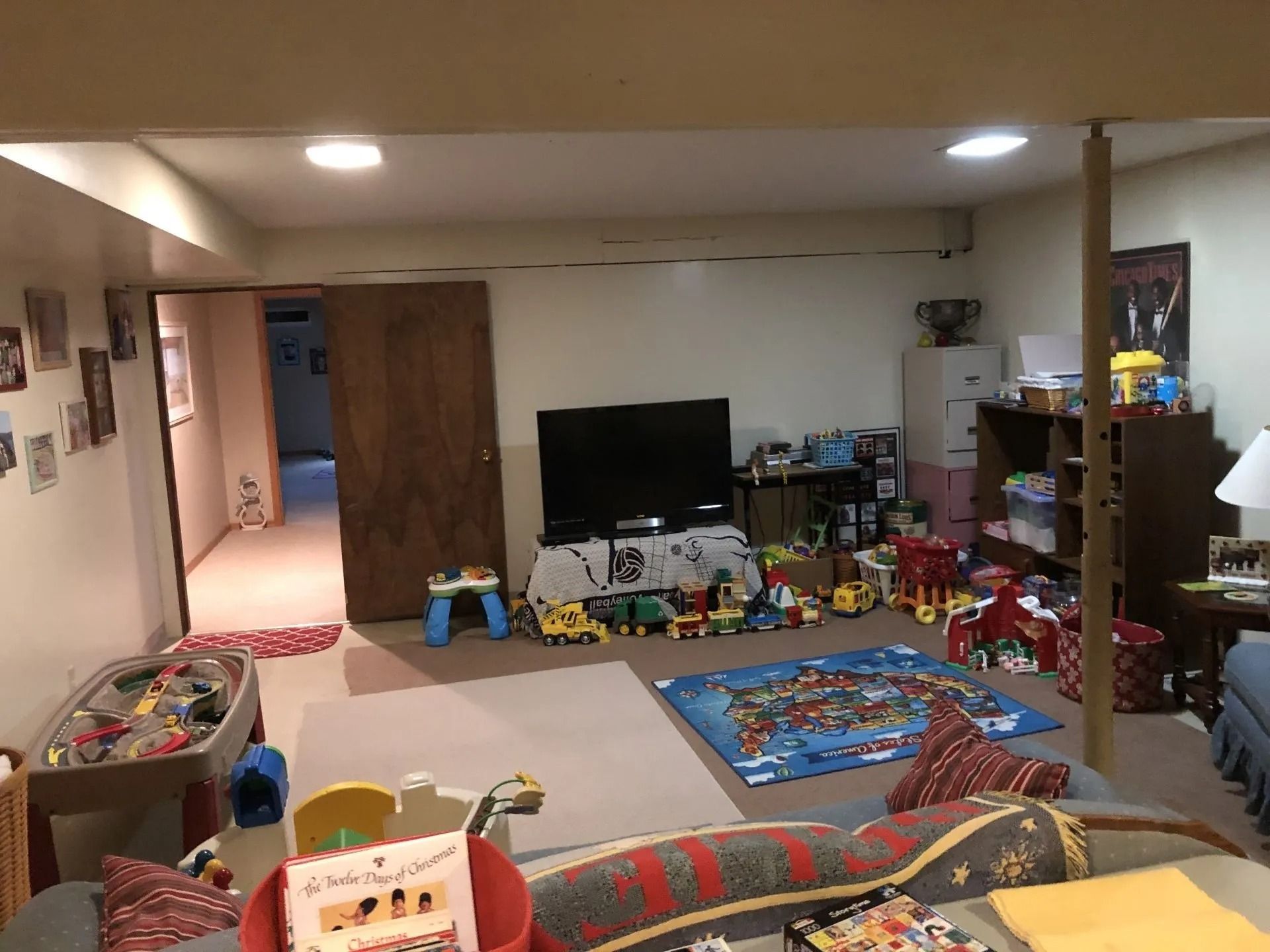 Cluttered family room with toys, TV, and couch in a basement-like living space