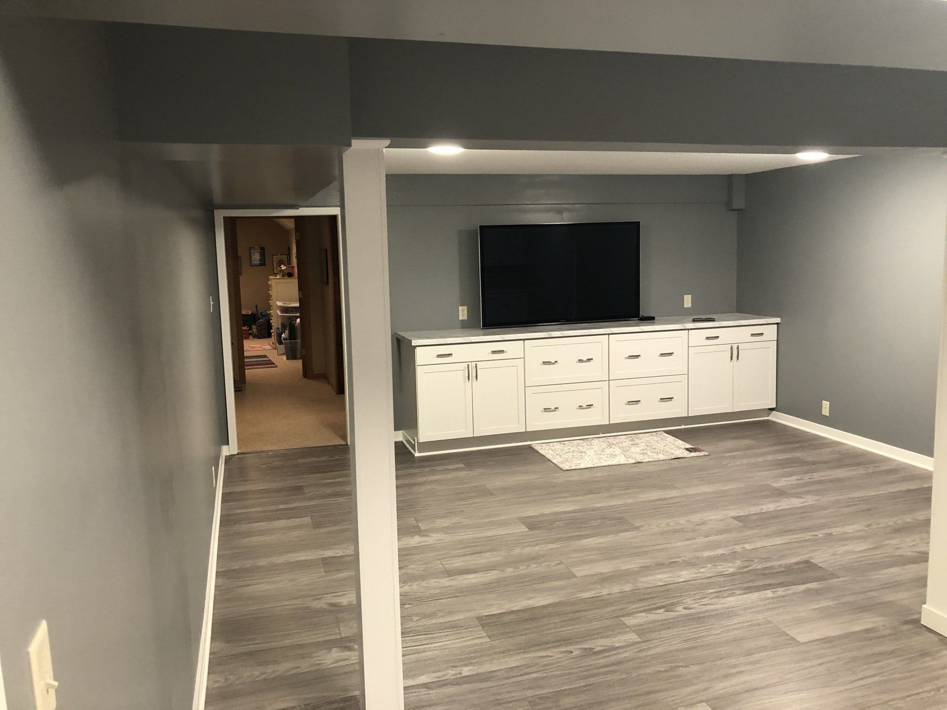 Finished basement with gray walls, white built-in cabinets, and a wall-mounted TV.