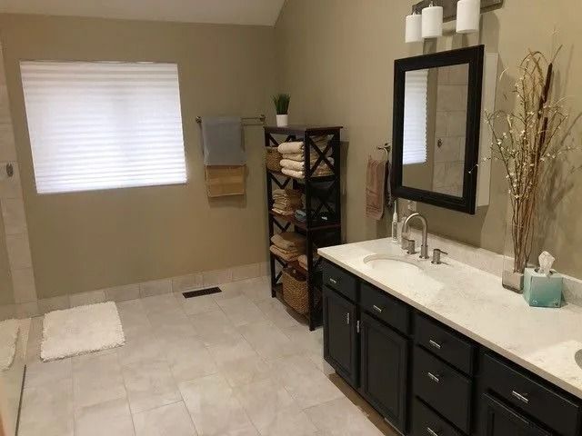 Modern bathroom with tiled floor, dark vanity, large mirror, shower area, and window with blinds
