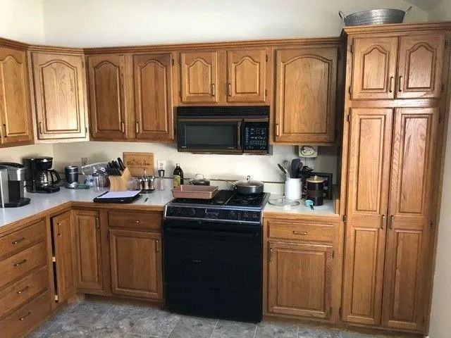 Kitchen with oak cabinets, black appliances, and countertops on two walls