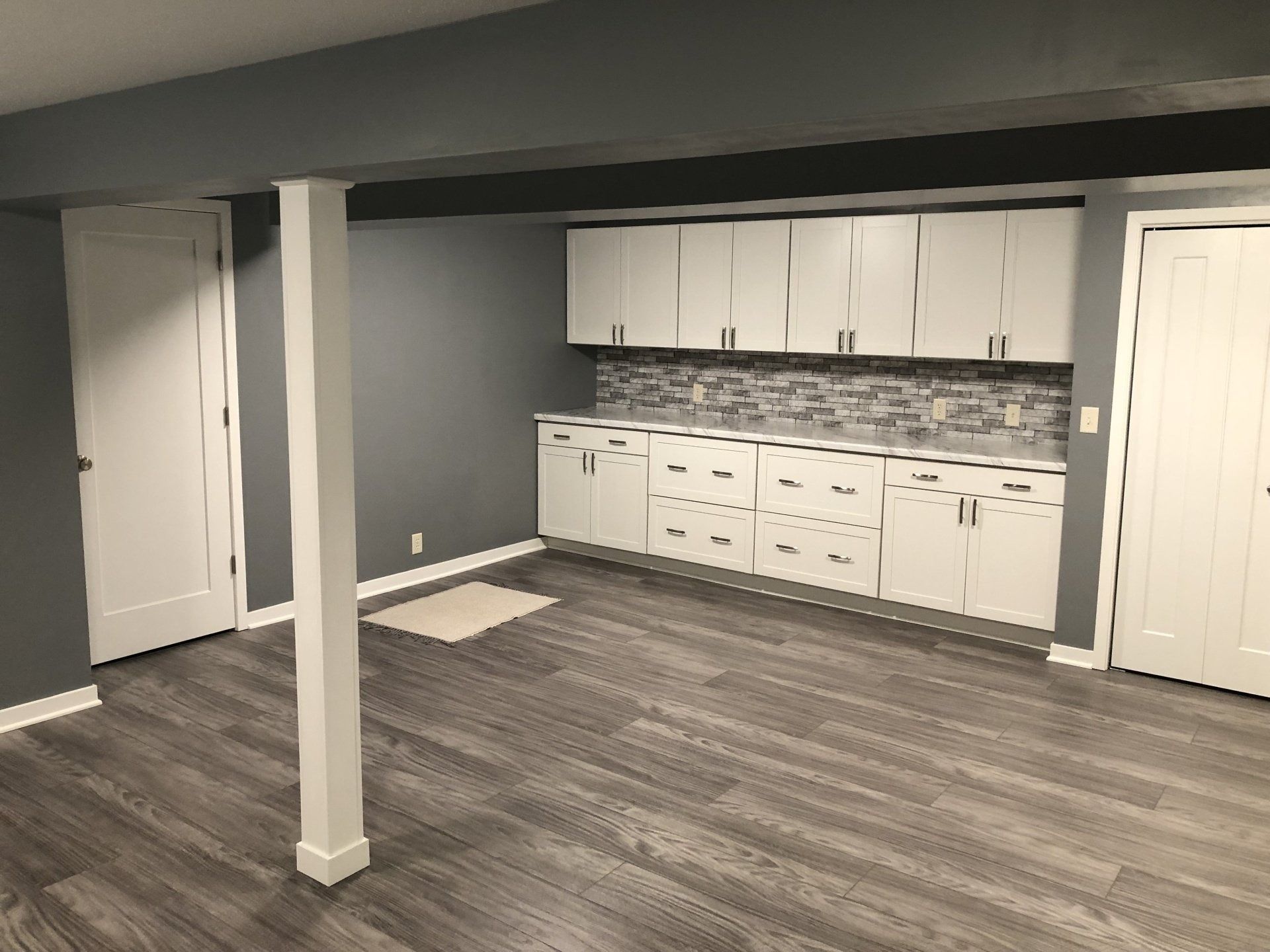 Empty finished basement room with gray walls, white cabinets, and dark wood-look flooring
