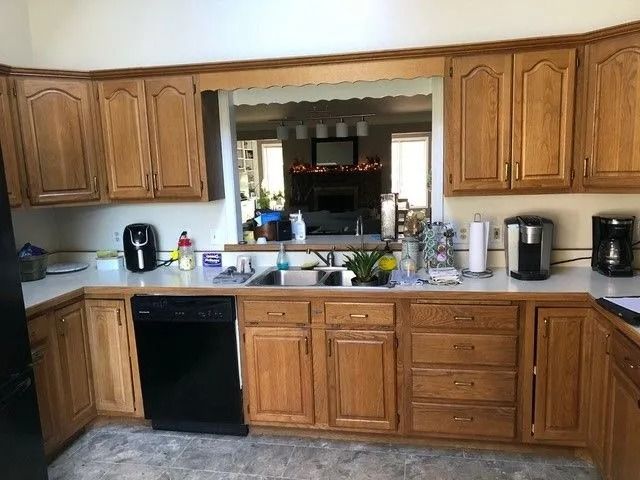 Kitchen with wooden cabinets, countertop clutter, sink, dishwasher, and coffee makers beside a pass-through window.