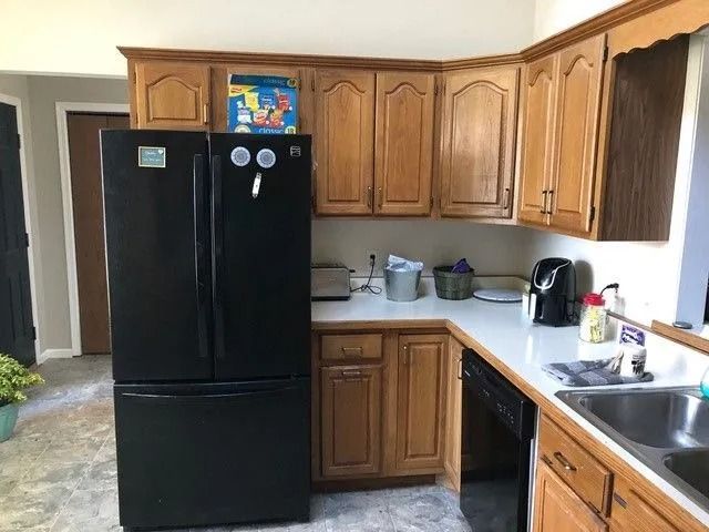 Kitchen with black refrigerator, wooden cabinets, double sink, and light countertops