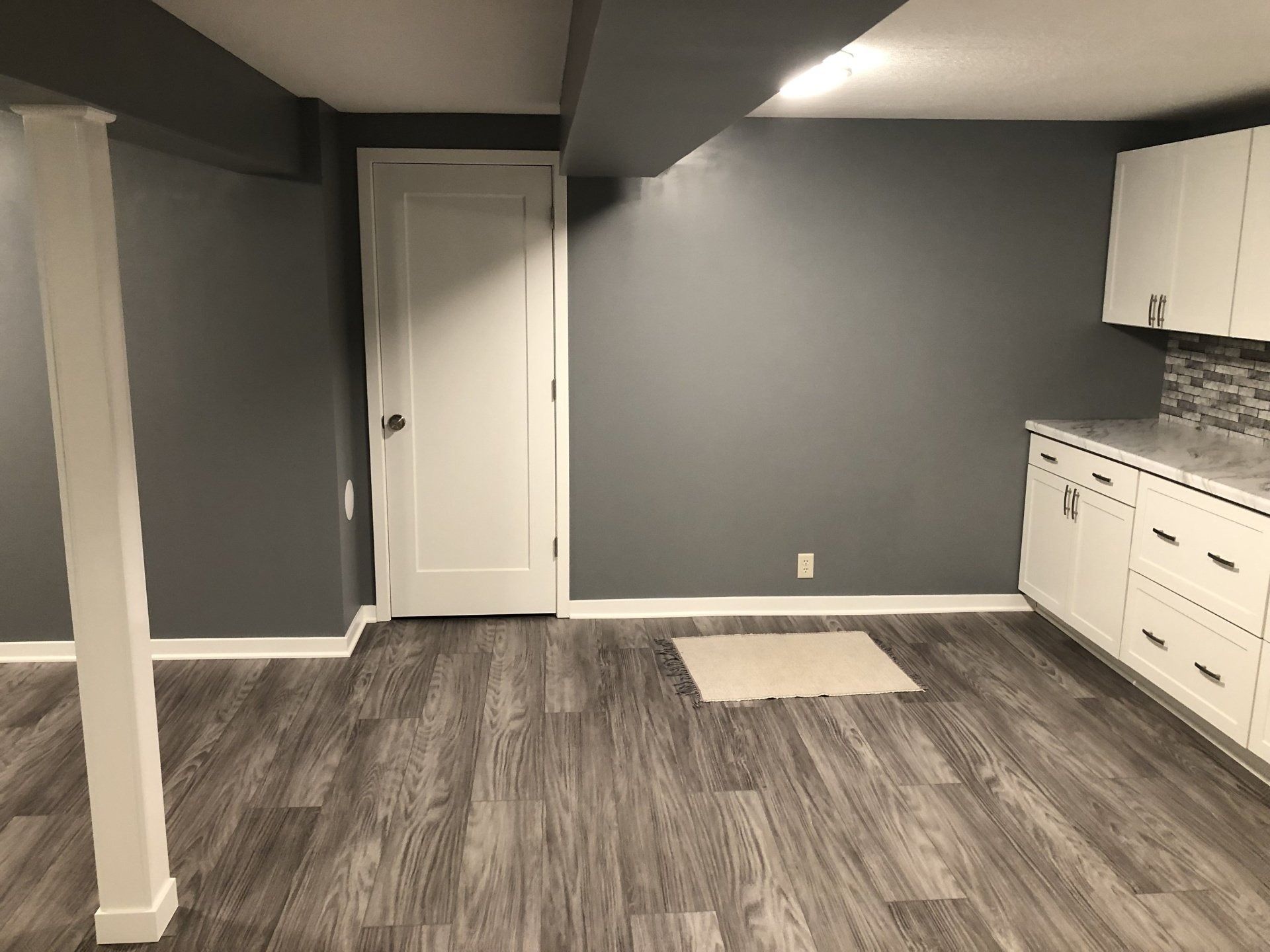 Empty gray basement room with white cabinets, door, and gray wood flooring