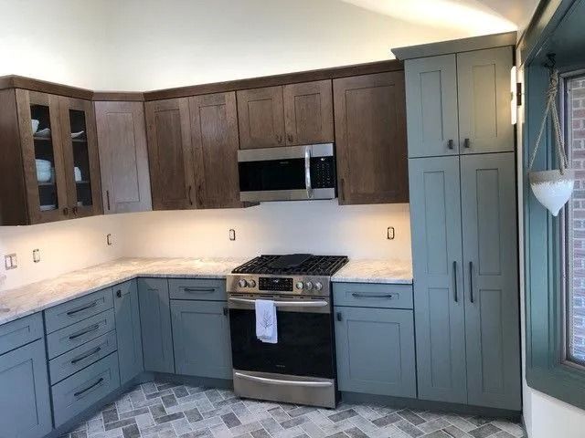 Modern kitchen with blue-gray cabinets, dark wood upper cabinets, stainless appliances, and a gas range.