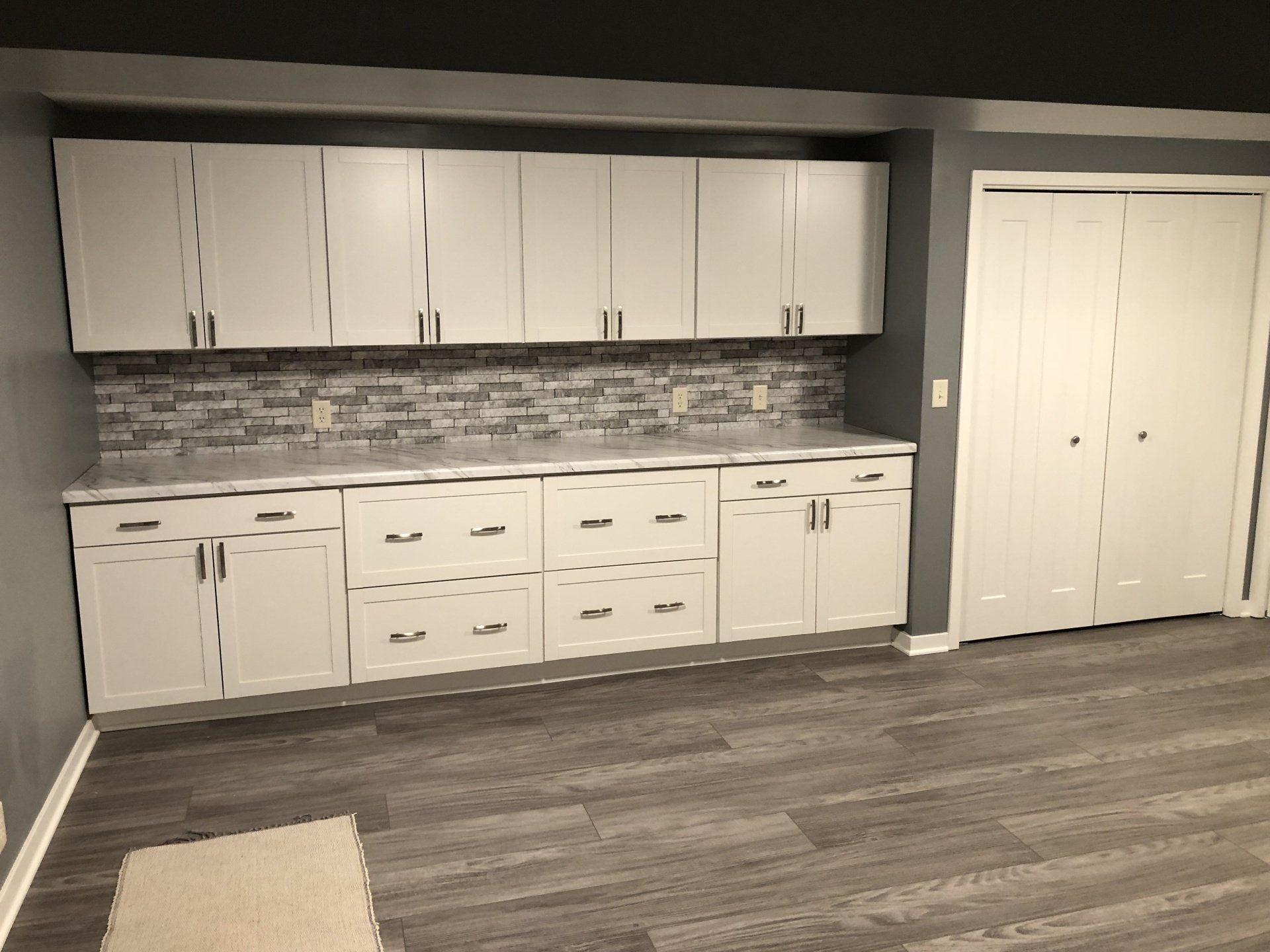 Kitchen with white cabinets, gray tile backsplash, and wood-look flooring beside double closet doors
