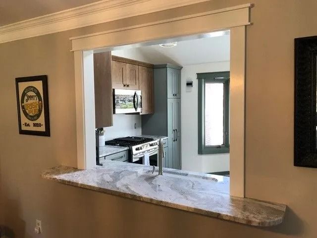 Interior view through a wide pass-through window into a kitchen with light cabinets and a stove.