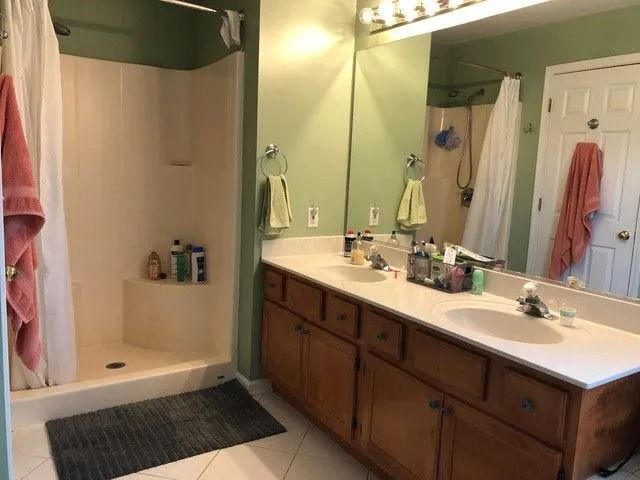 Bright bathroom with shower stall, double vanity, mirrors, towels, and dark bath mat.